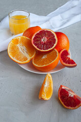 Sweet and juicy blood oranges and oranges, whole and cut on a white plate and glasses of fresh...