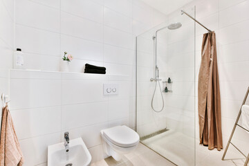 Modern interior of washroom with glass shower cabin and white hung wall toilet with bidet