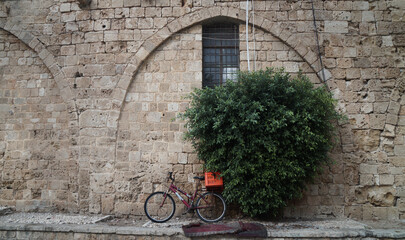 Fototapeta na wymiar an old bicycle resting on a large stone wall next to a bush, in Akko, Israel