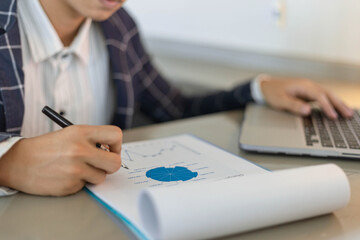 Business partners concept a young businessman using a laptop revising annual sales summary