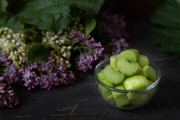 Rhabarber in Stücke geschnitten in einer Schale auf dunklen, rustikalen Untergrund aus Holz mit Flieder im Hintergrund
