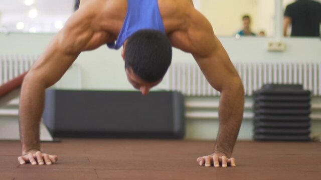 Close up to muscular man doing push ups in handstand at gym. Young athlete in sportswear doing stunts indoor. Strong sportsman showing performance. Healthy and active lifestyle concept. Slow motion
