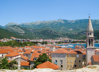 View from the top of fortress on the Budva Riviera-the old town, houses with tiled roofs, the sea bay with white yachts. And a city on the background of green mountains