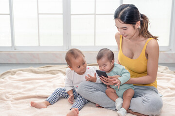 Young Asian beautiful mother watching a photo or video clip from mobile phone with 2 little children. Mother having a happy time with her babies.