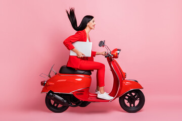Fototapeta na wymiar Full size profile side photo of young smiling beautiful woman riding moped with laptop isolated on pink color background