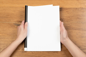Woman holding brochure with blank cover on wooden background, top view. Mock up for design