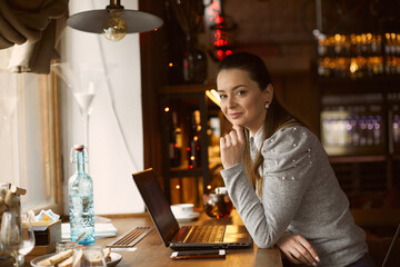A young beautiful woman a girl who ordered tea in a cafe in a cafe sits at a table looking at the camera and smiles. Combining useful and pleasant