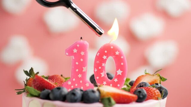 Birthday cake candle number 10. Candle and cake on pink background and fire by lighter. Close-up and slow motion