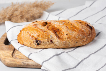 Freshly baked, yeast-free, whole wheat flour bread with cranberries. Served on a wooden board with a knife on a kitchen towel. Light kitchen background. Homemade baking