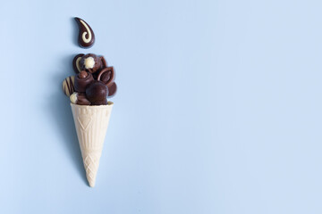 Delicious chocolate pralines in waffle cone on blue background with copy space. World Chocolate Day concept