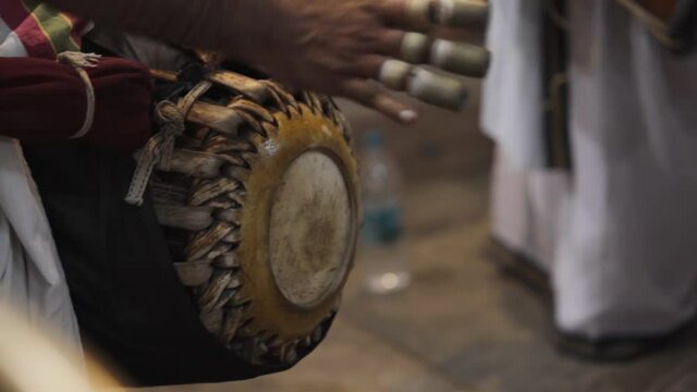 A close up shot of male devotee or Hindu priest playing devotional music using traditional instruments khol or drums or tabla while celebrating ritual or festival in a south temple