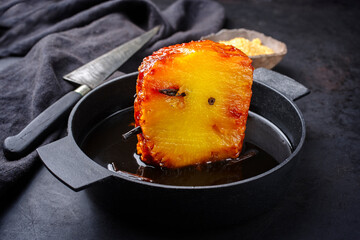 Backed caramelized pineapple with vanilla caramel sauce as top view on a modern design cast iron pan with copy space