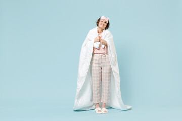 Fototapeta na wymiar Full length young confused woman in pajamas jam sleep eye mask rest relax at home wrap cover under blanket duvet look overhead isolated on pastel blue background studio Bad mood night bedtime concept.