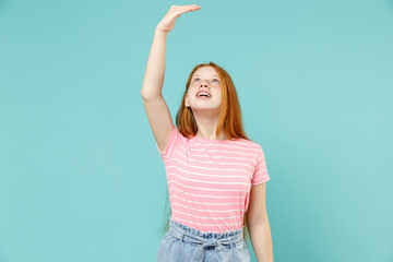 Little redhead kid girl 12-13 years old in pink striped t-shirt hold hand above head show how much...
