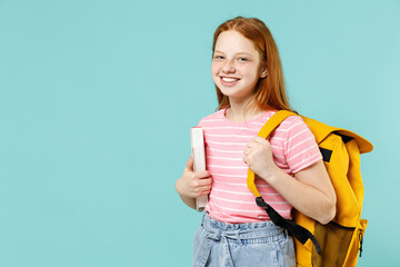 Little smart happy pupil redhead kid girl 12-13 year old in pink striped t-shirt hold notebook book yellow school bag backpack isolated on pastel blue background Children lifestyle childhood concept. - obrazy, fototapety, plakaty