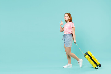 Full length traveler tourist kid girl 12-13 year old in pink t-shirt hold suitcase show thumb up isolated on pastel blue background Passenger travel abroad weekends getaway Air flight journey concept