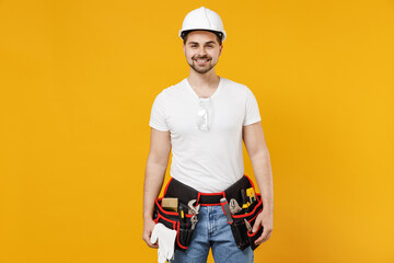 Young smiling fun employee handyman man 20s wearing protective helmet hardhat isolated on yellow background studio portrait. Instruments accessories for renovation apartment room. Repair home concept