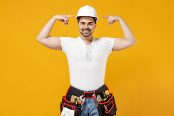 Young happy smiling employee handyman man in protective helmet point index finger on hardhat isolated on yellow background. Instruments accessories for renovation apartment room. Repair home concept
