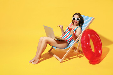 Full body length happy young woman wear red blue one-piece swimsuit sit on chair work hold laptop...