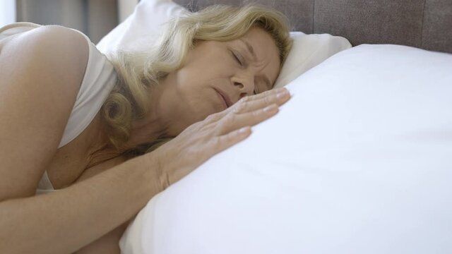 Depressed mature widow lying in bed, touching empty pillow, feeling lonely