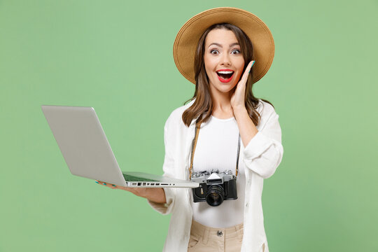 Traveler shock amazed tourist woman in casual clothes hat camera usig laptop pc computer hold face isolated on green background Passenger travel abroad on weekends getaway. Air flight journey concept.