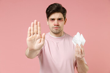 Sick ill allergic man has red watery eyes runny nose suffer from terrible allergy hold paper tissue napkin isolated on pastel pink color background. Pollen allergy symptoms seasonal rhinitis concept