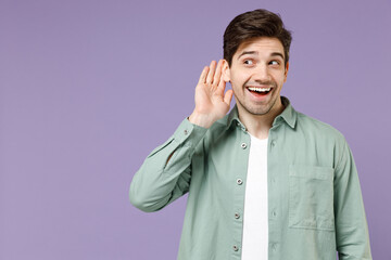 Young cerious nosy caucasian man 20s wearing mint shirt white t-shirt try to hear you overhear listening intently look aside isolated on purple background studio portrait. People lifestyle concept