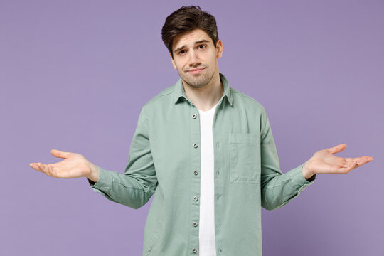 Young sad mistaken confused displeased man 20s years old wearing casual mint shirt white t-shirt spread hands arms oops gesture isolated on purple violet background studio. People lifestyle concept