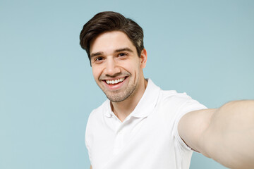 Close up young smiling caucasian man 20s wearing white casual basic t-shirt doing selfie shot on mobile cell phone camera isolated on pastel blue background studio portrait People lifestyle concept.