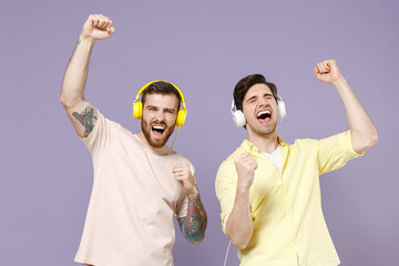 Two young happy men friends together 20s wearing casual t-shirt headphones listen to music dancing...
