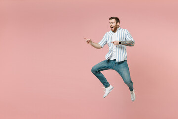 Fototapeta na wymiar Full length young joyful unshaven man wear blue striped shirt white t-shirt jump high point index finger aside on copy space workspace area isolated on pastel pink background. Tattoo translate fun