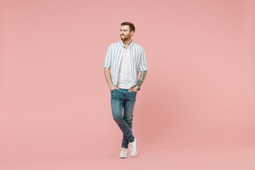 Fototapeta premium Full length young happy dreamful friendly caucasian unshaven man 20s in blue striped shirt white t-shirt look aside isolated on pastel pink color background studio portrait. People lifestyle concept.