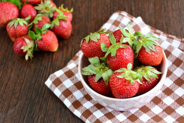 fresh strawberries in a pink bowl on the tablecloth on the wooden background