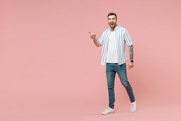 Full length young happy smiling caucasian unshaven man 20s in blue striped shirt point index finger aside on workspace area isolated on pastel pink color background studio. People lifestyle concept.