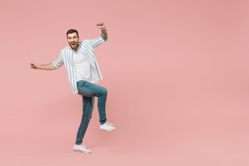 Fototapeta na wymiar Full length young excited overjoyed caucasian unshaven man in blue striped shirt clench fist do winner gesture with raised up leg isolated on pastel pink background studio People lifestyle concept