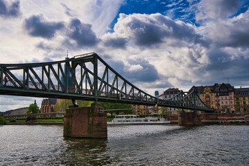 Fotografie vom eisernen Steg in Frankfurt vor einem blauen, aber sehr wolkigen Himmel.