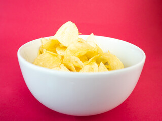 Potatoes chips in white bowl on red background