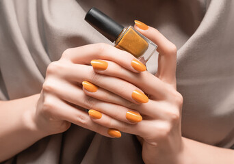 Female hands with orange nail design. Glitter orange nail polish manicure. Woman hold orange nail polish bottle. - obrazy, fototapety, plakaty