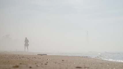 Fototapeta na wymiar People walking on the beach in the fog. Sunny, hot summer day, but cold water. Pavilosta, Latvia.