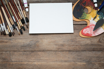 Blank canvas, brushes, palettes and paints on wooden table, flat lay. Space for text
