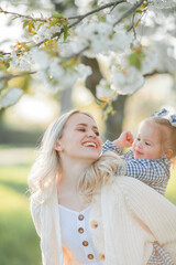 A beautiful young mother with her little daughter are resting on a picnic in the flowering garden. White flowers. Spring. Happiness.