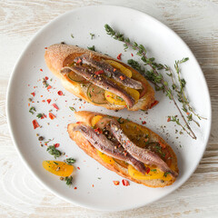 bruschettas with tomatoes, anchovies and thyme on a white plate on a light wooden table