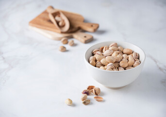 Pistachio nuts in a white bowl on a white  marble background. Front view and copy space