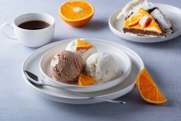 Vanilla and chocolate ice cream, cake and orange slices on a light wooden table