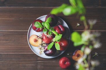 a few juicy red plums in blue plate with branch blossom flowers on a napkin on a brown wood background. Top view and copy  space