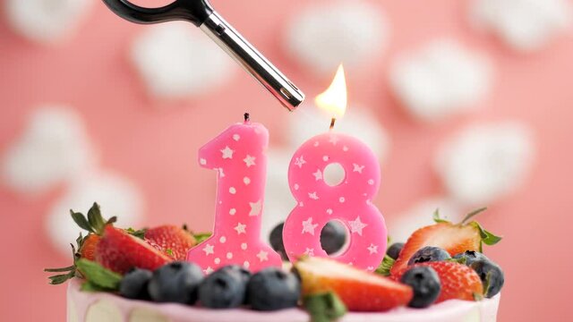Birthday cake candle number 18. Candle and cake on pink background and fire by lighter. Close-up and slow motion