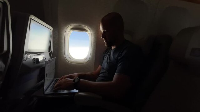 Man working on his laptop while flying in the airplane