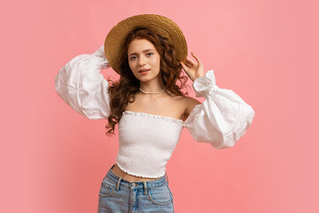 Happy Woman in summer outfit plays hair on pink background. Straw hat, white top with sleeves, natural make up.