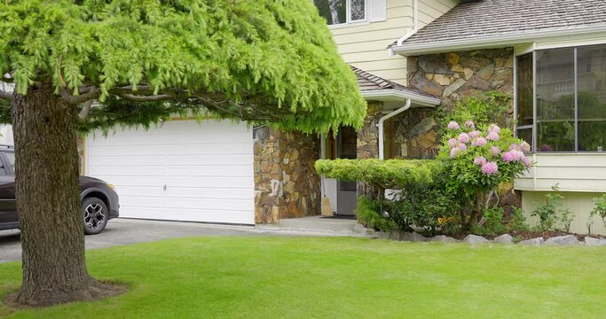 Establishing shot of two story stucco luxury house with garage door, big tree and nice landscape in Vancouver, Canada, North America. Day time on May 2021. ProRes 422 HQ.