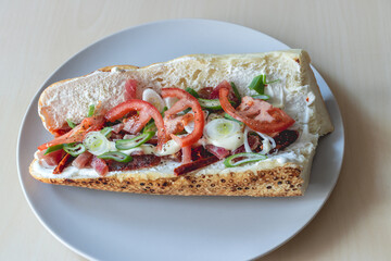 Sandwich in half a muffin with spring onions, tomatoes, ham and sour cream served on a gray plate